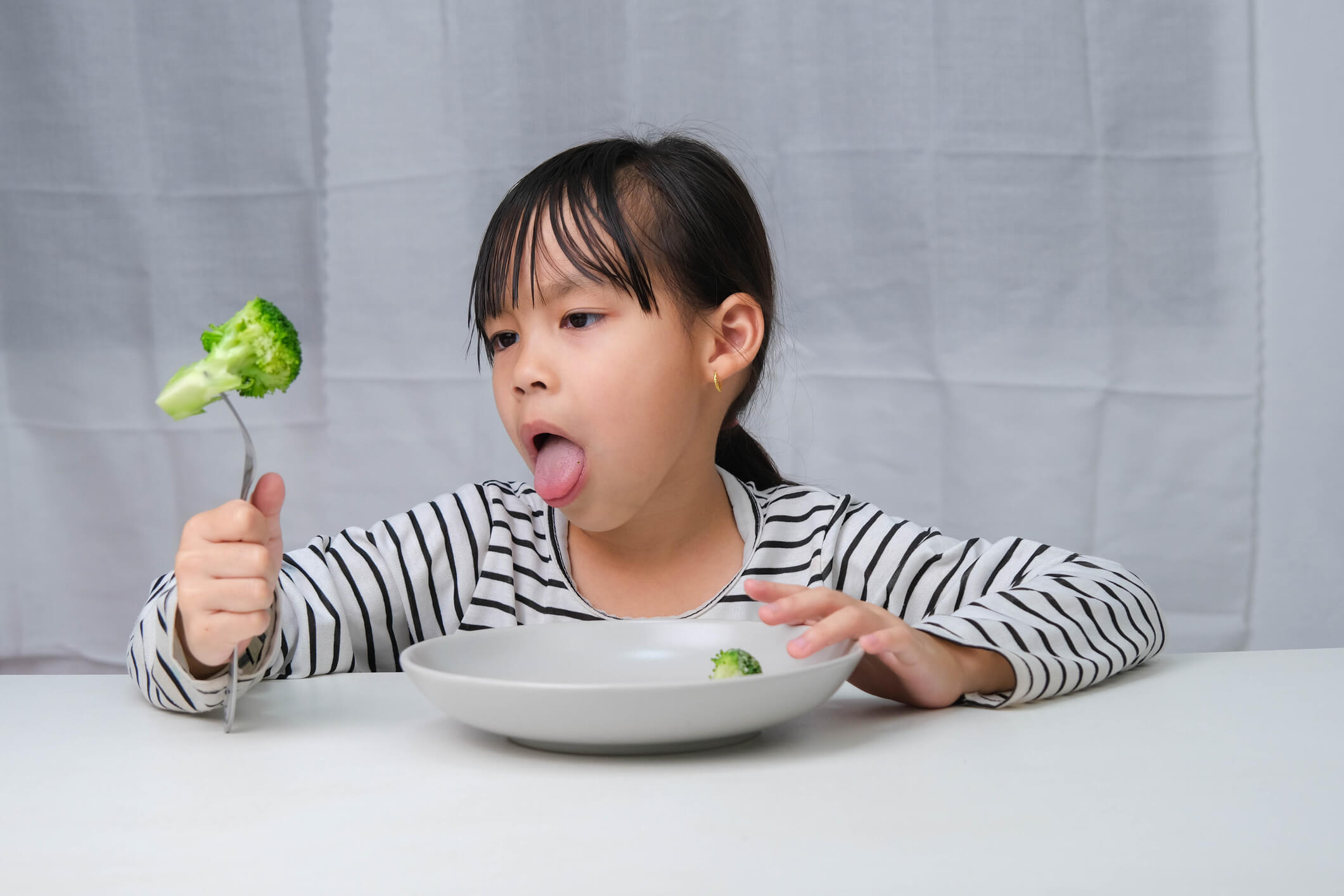 Petite fille qui hésite à manger un brocolis